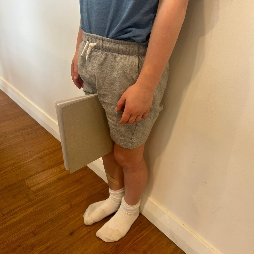 A boy standing against a wall with a book between his legs illustrating how to size a kids bike using inseam measurement