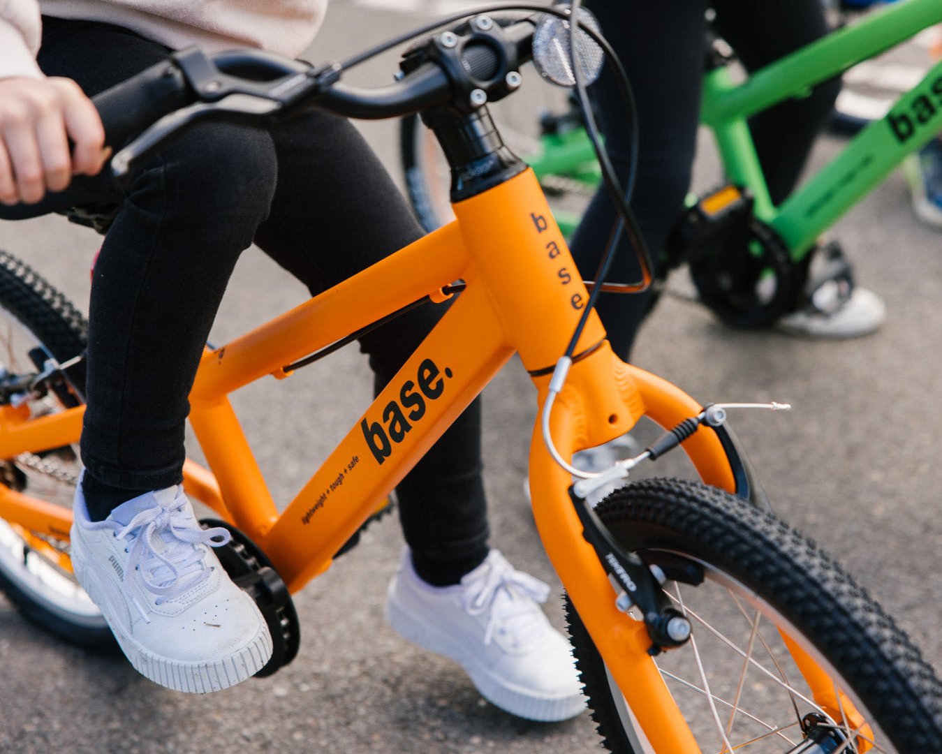 Two kids bikes on a pavement with kids on them ready to take off