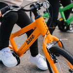 Two kids bikes on a pavement with kids on them ready to take off
