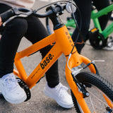 Two kids bikes on a pavement with kids on them ready to take off