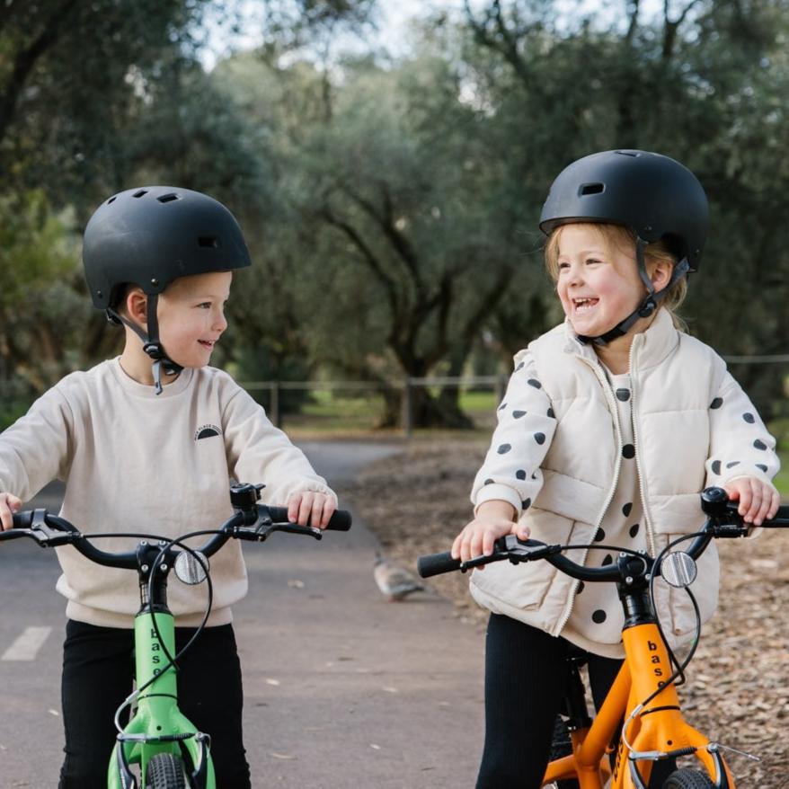 A girl and a boy smiling and standing over their 16 inch kids bikes on a pretty path