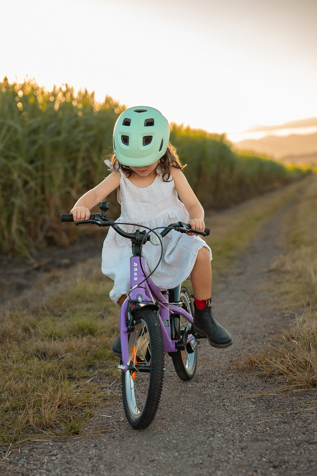 Child riding a bicycle on a dirt path with cornfields in the background
