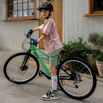 A child wearing a black giro helmet, stands over to a green and black mountain bike.