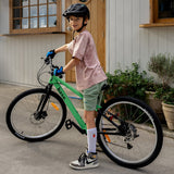 A child wearing a black giro helmet, stands over to a green and black mountain bike.