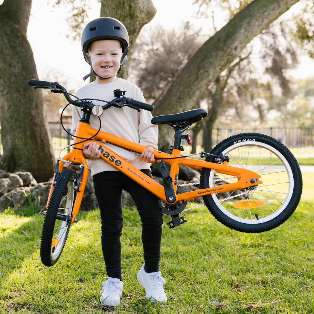 5 year old smiling while lifting a 16 inch kids bike by a tree