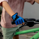 A close-up of a person wearing a bright blue and black cycling glove while gripping the handlebar of a green bicycle.