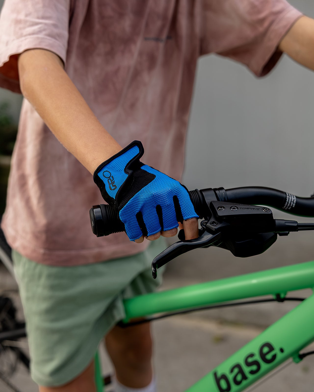 A close-up of a person wearing a bright blue and black cycling glove while gripping the handlebar of a green bicycle.