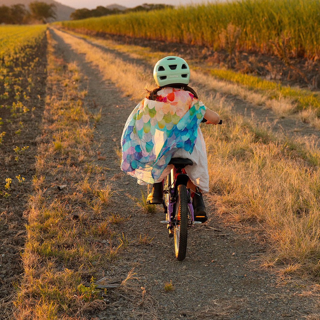 Child riding a bike on a dirt path with a colorful coat and helmet.