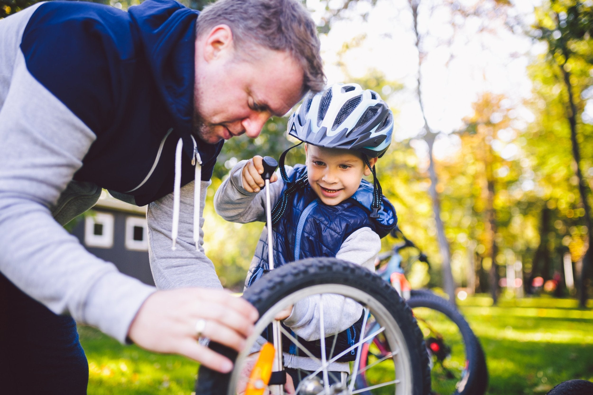 Father and child smiling while maintaining a kids bike. The bike is upside down and the dad and child have tools.