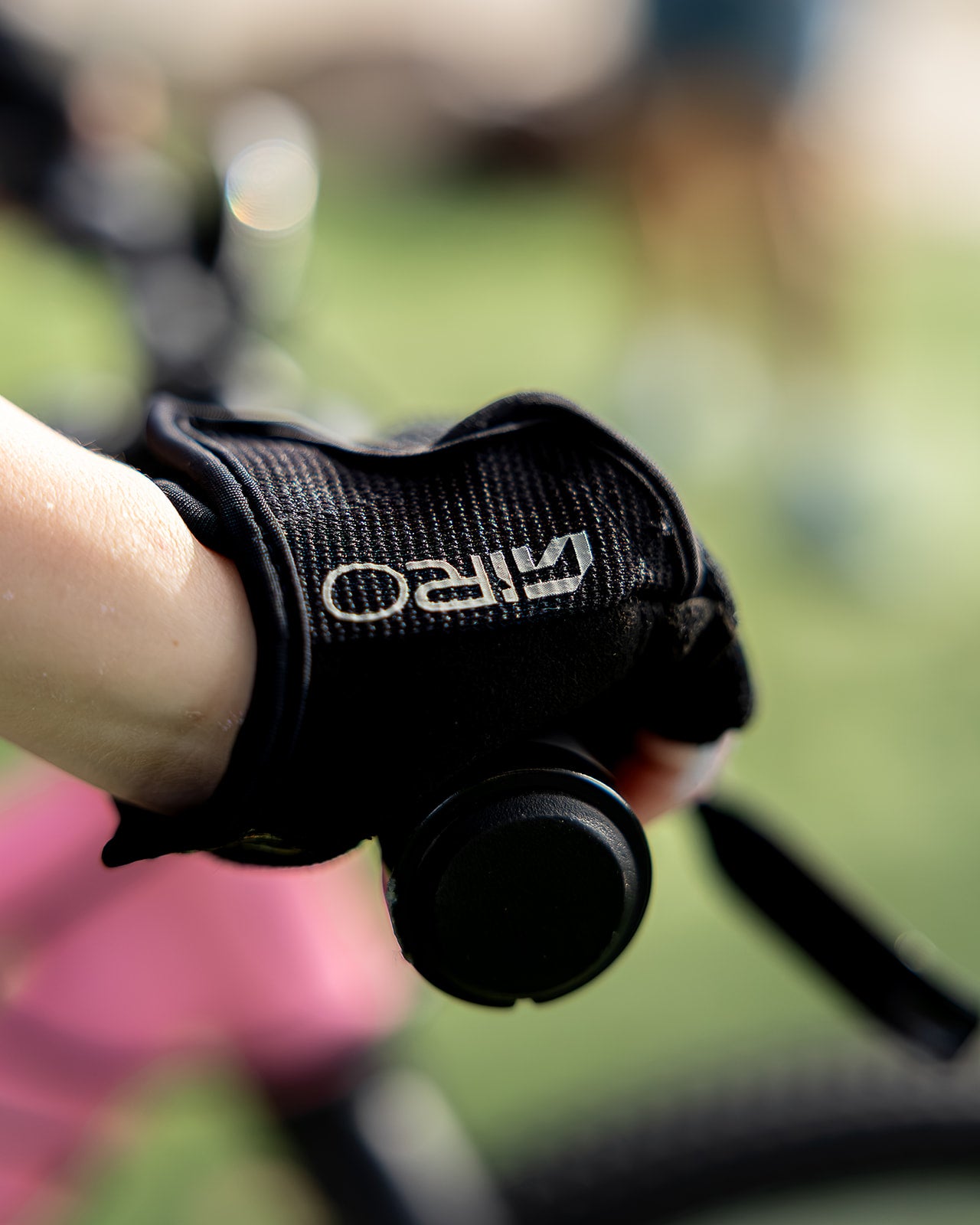 A close-up of a person's hand wearing a black Giro fingerless glove while holding a bicycle handlebar, with a blurred outdoor background.