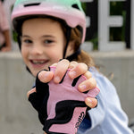 A child wearing a Giro helmet and pink and black fingerless cycling gloves, with the child's hands prominently featured in the foreground against a blurred outdoor background.