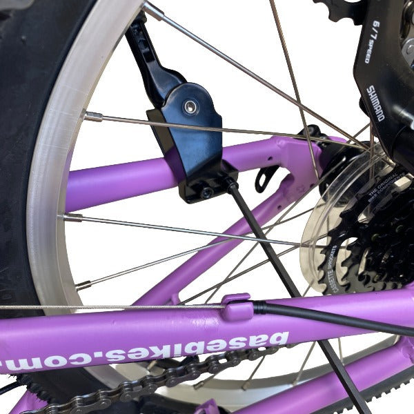 Close-up of a lilac bicycle frame and rear wheel with a black derailleur and chain guard. The frame has white text reading 'basebikes.com.au'