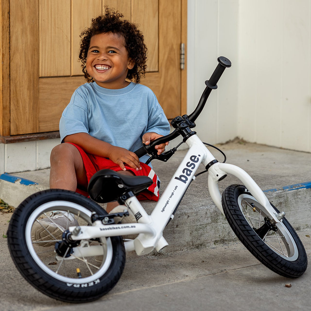 A smiling young child sits by a white balance bike.