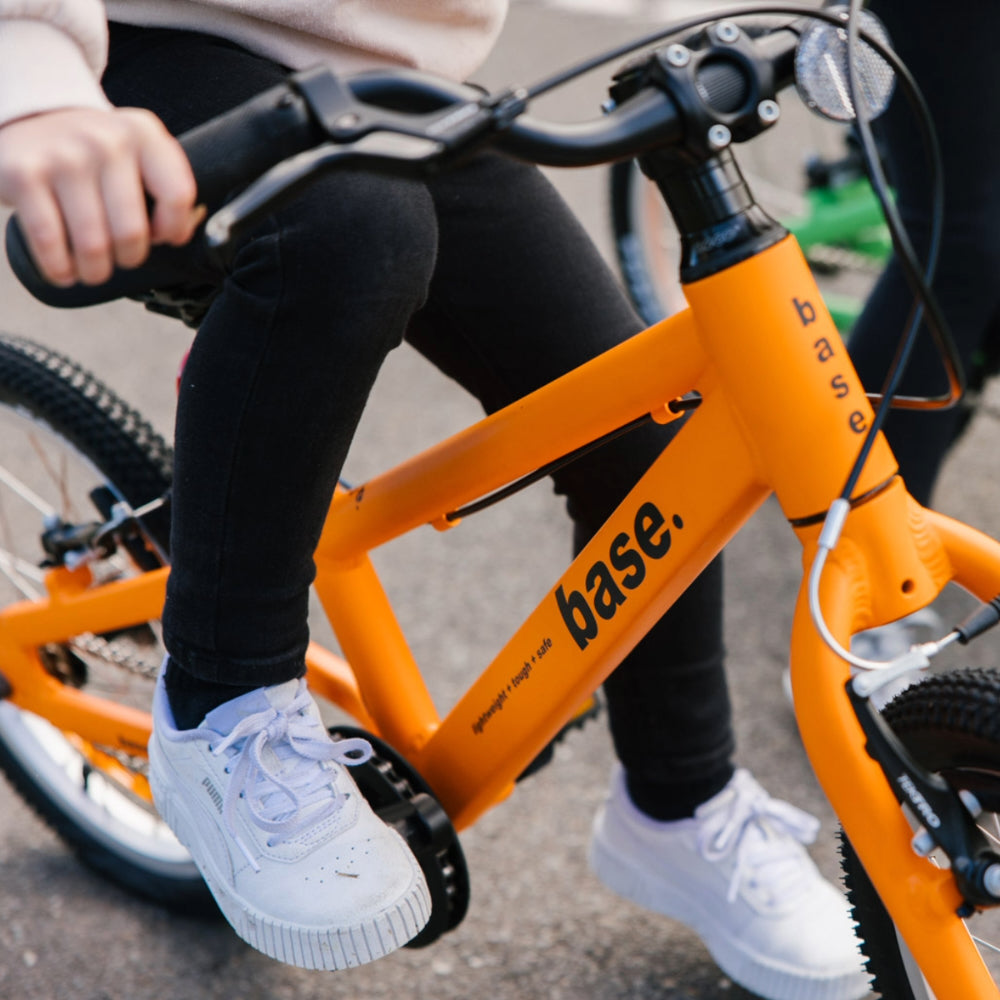 Close up of orange 16 inch kids bike with 5 year old on the saddle with her foot on the pedal