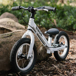 White base balance bike propped up against a log