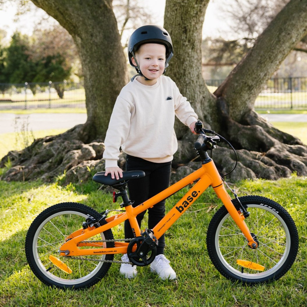 Young boy smiling next to his orange base bike