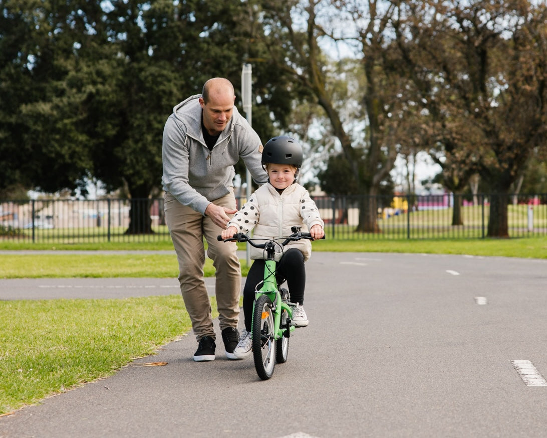 Young girl learning to ride on a 16 inch kids bike with her dad running along side