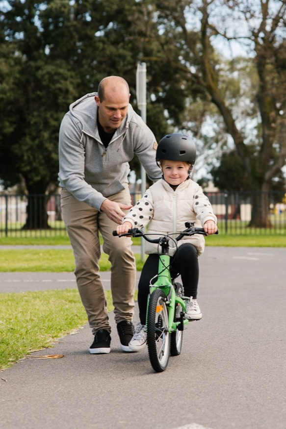 Dad helping child learn to ride on a green bike