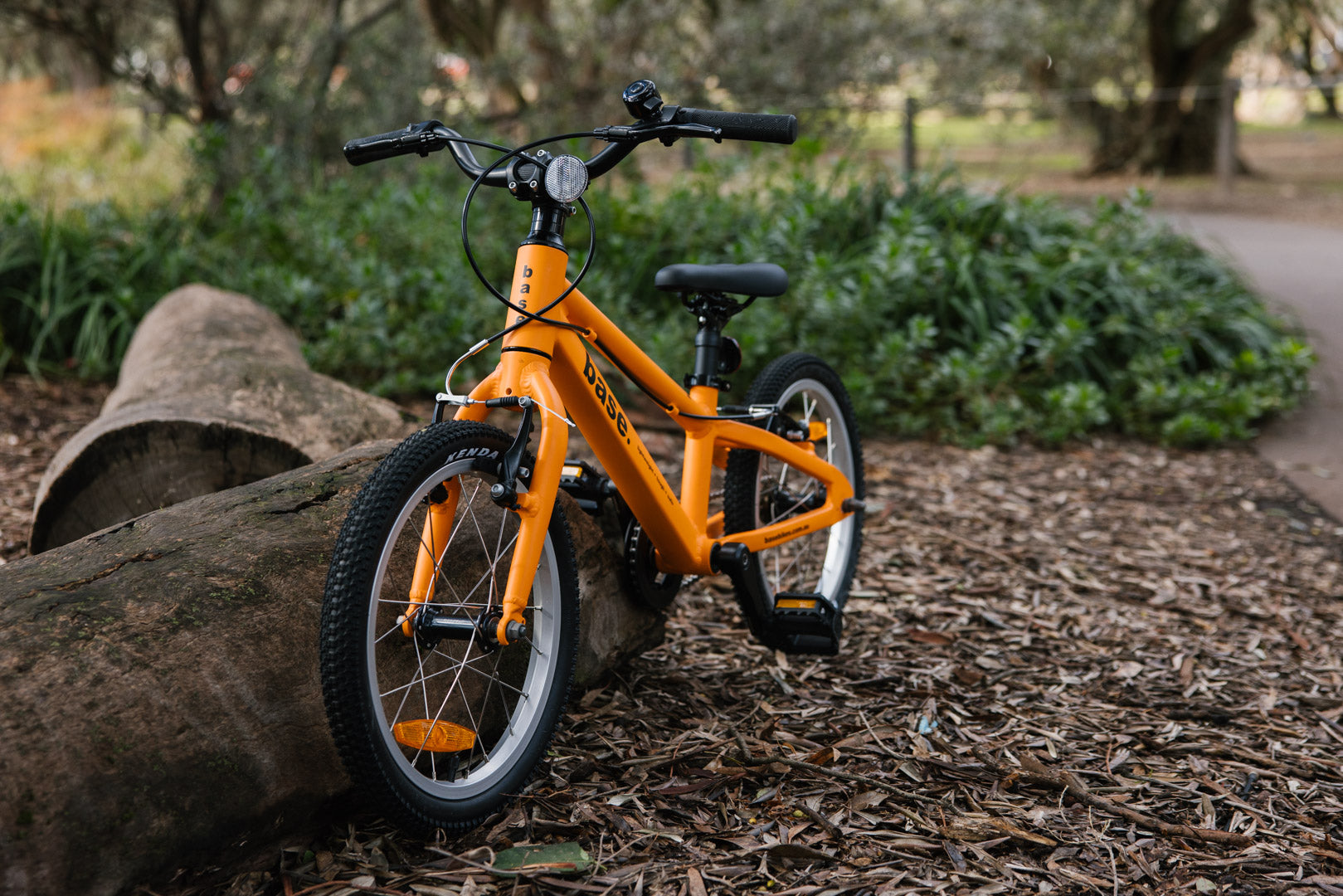 Orange kids base bike propped against a log in a wooded area