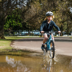Young boy riding his blue 20 inch bike through a large puddle creating a splash
