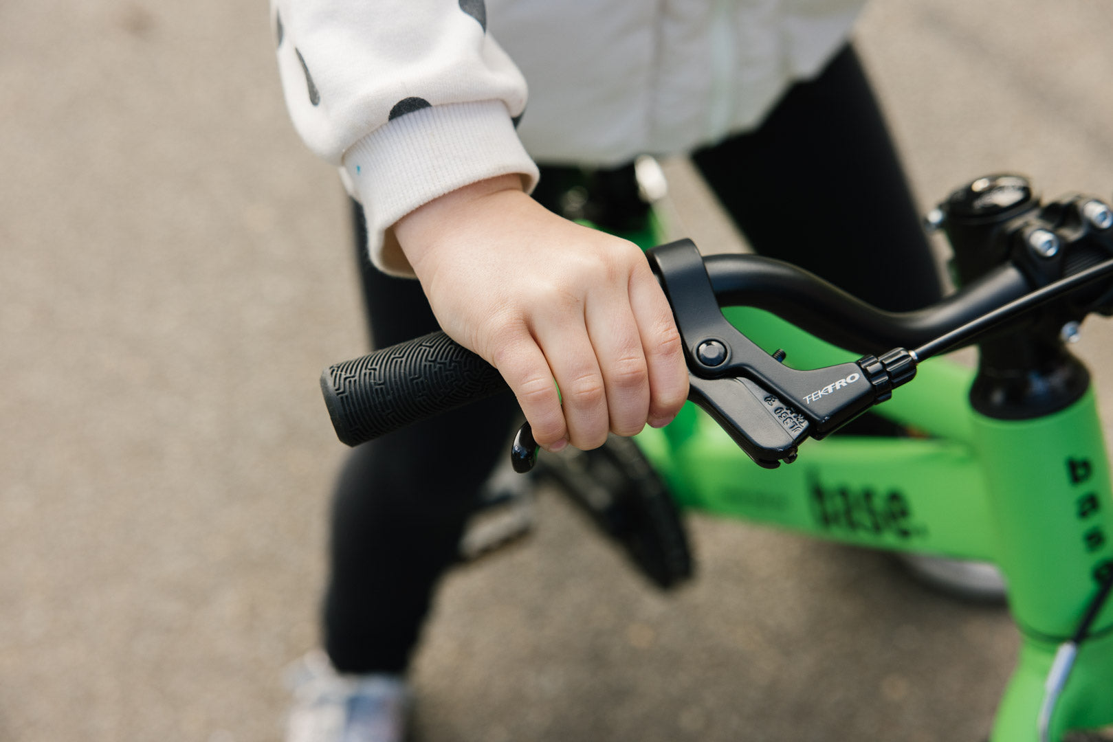 Young girl squeezing the brake lever on her green base bike