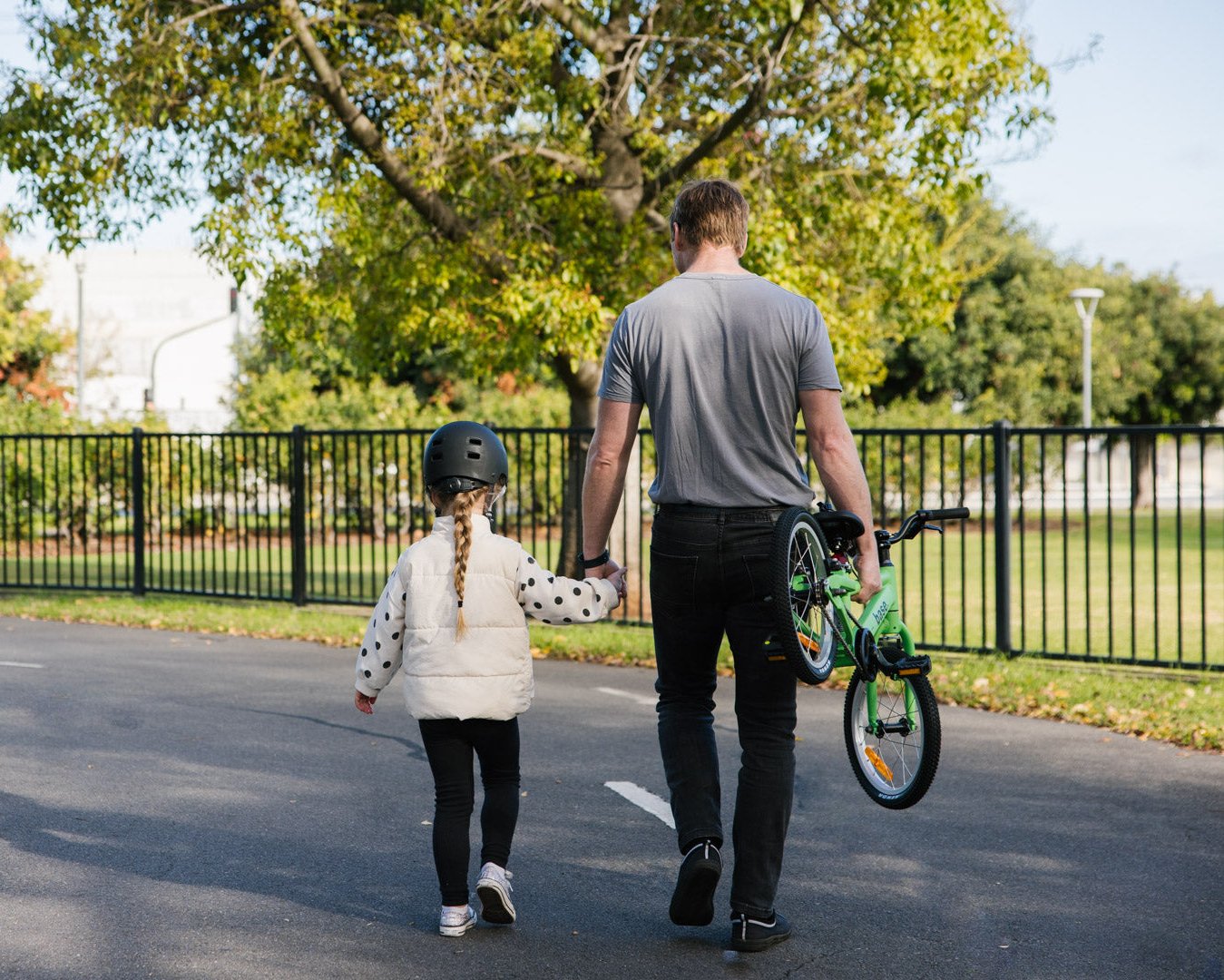 Photo from behind of dad holding kids hand and carrying the kids bike