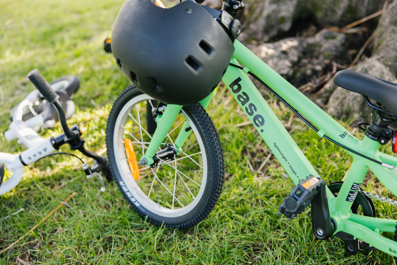 Green base 16 kids bike on a lawn with bike helmet on the handlebar