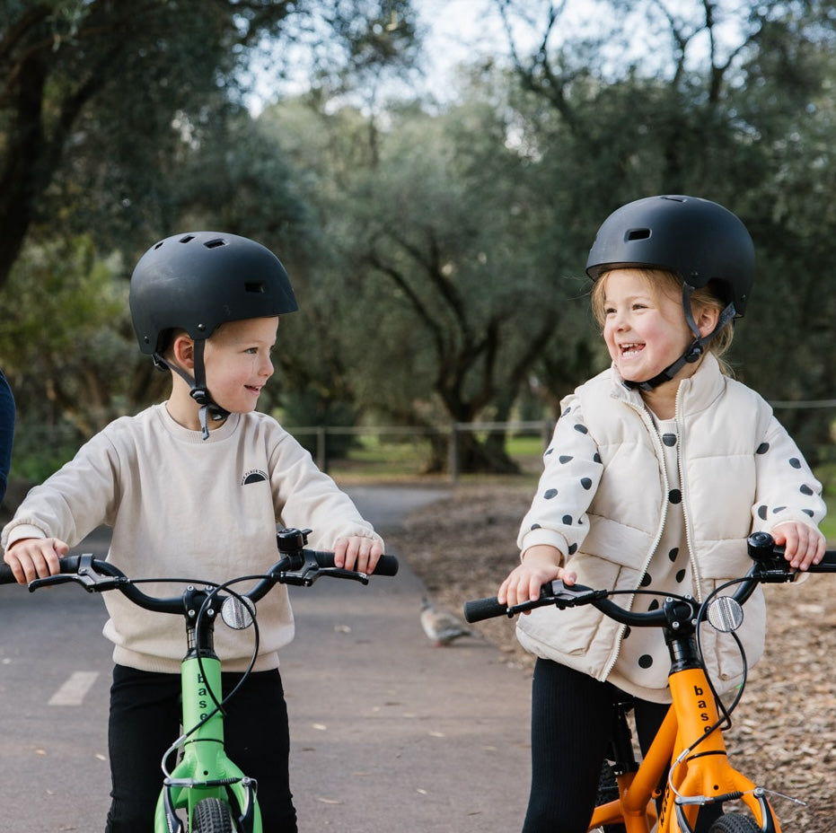 Two smiling kids standing over their base bikes on a pretty path