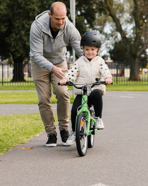 Dad teaching child to learn to ride a bike in a learn to ride area